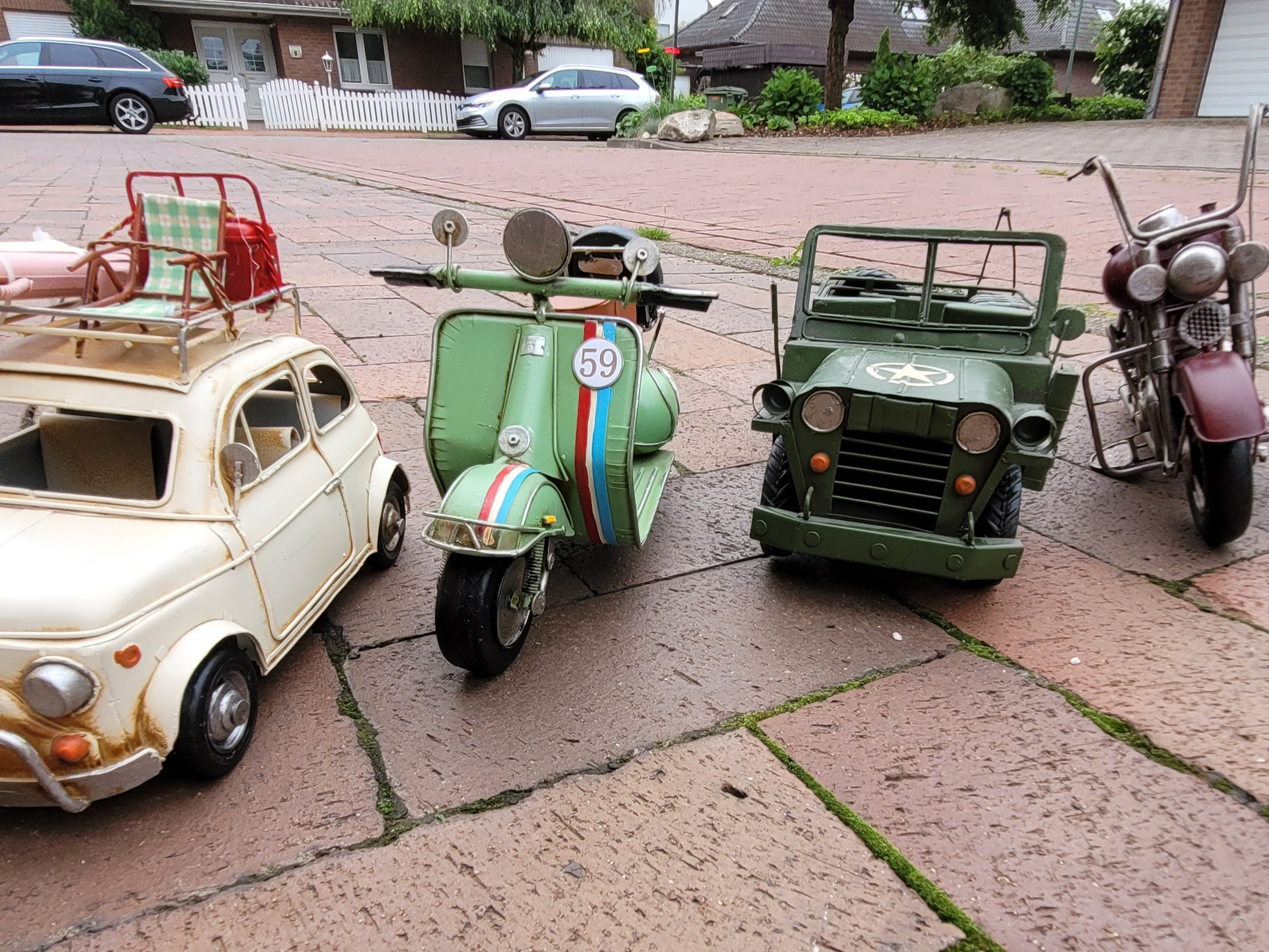 Deko-Modelle von Oldtimer-Auto, Vespa-Roller und Militärjeep auf Pflastersteinen