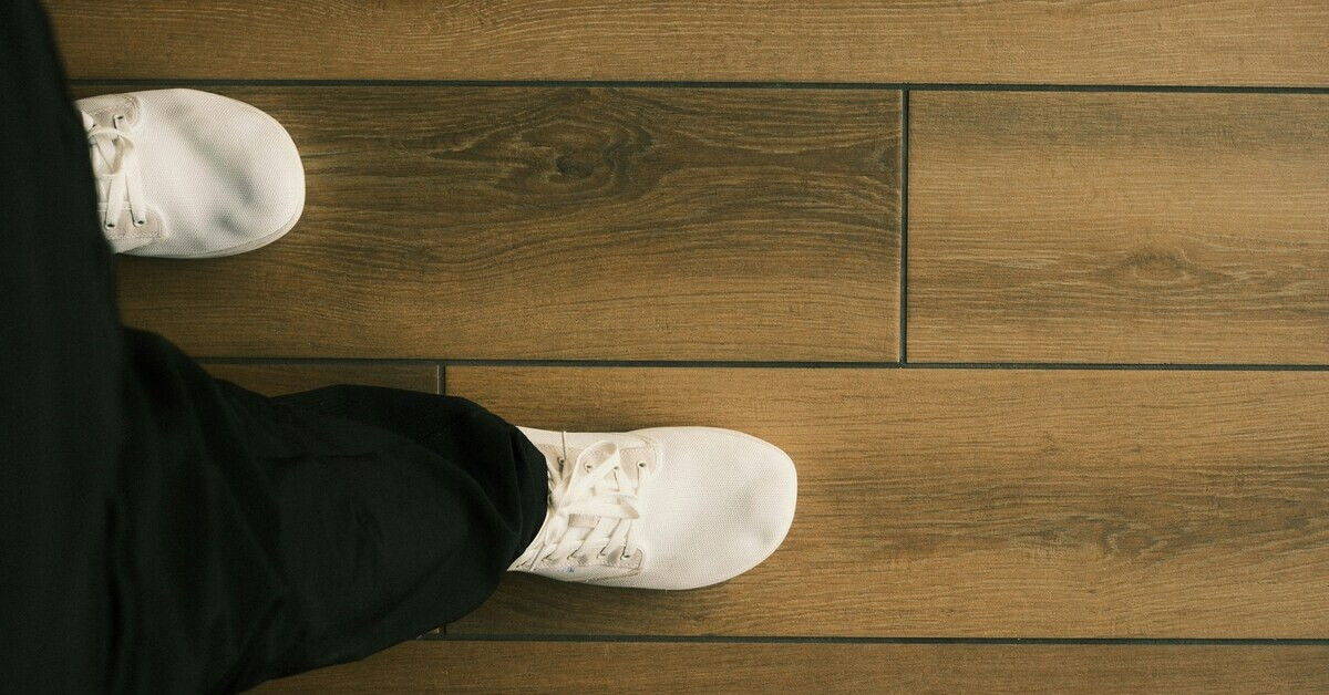 Parkett über Fliesen verlegt – Nahaufnahme eines Holzfußbodens mit Schuh