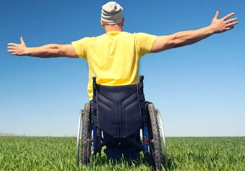 Mann im Rollstuhl mit ausgebreiteten Armen auf einer Wiese unter blauem Himmel – Symbolbild für Barrierefreiheit und Lebensfreude, passend zur Startseite und Öffnungszeiten