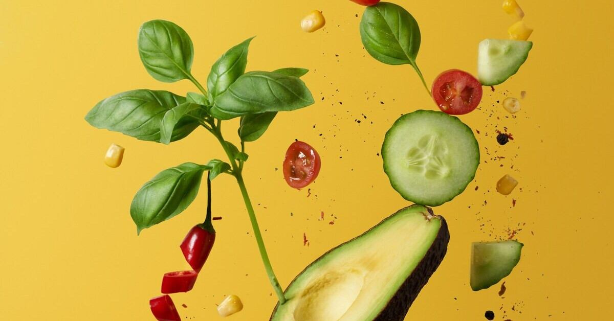 Frisches Obst und Gemüse auf gelbem Hintergrund mit Avocado, Gurke, Tomaten und Basilikum.