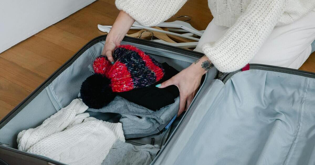Frau packt einen Koffer mit Kleidung und Mütze