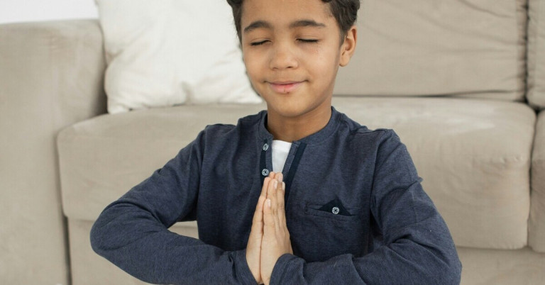 Junge bei der Meditation – Kind meditiert mit gefalteten Händen Junge bei der Meditation mit gefalteten Händen im Wohnzimmer
