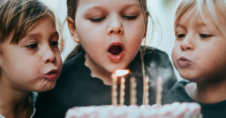 Kinder pusten Kerzen auf einem Geburtstagskuchen aus