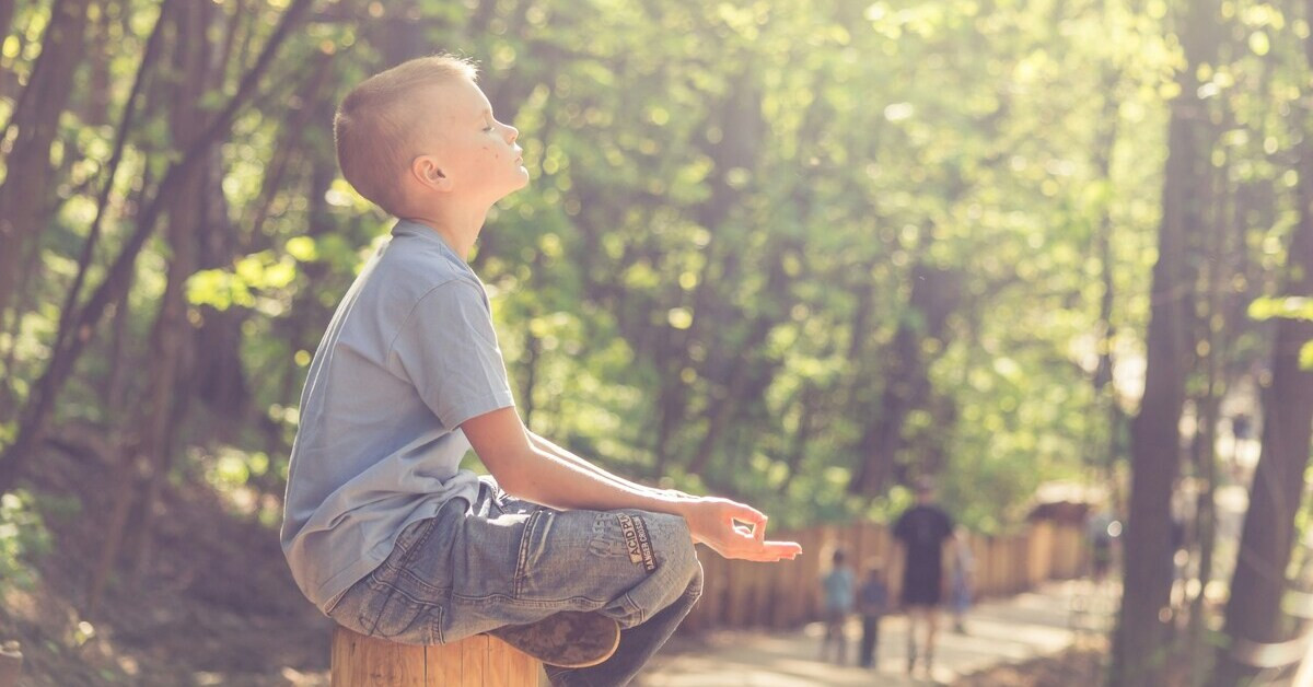Entspanntes Kind sitzt meditierend im Freien an einem sonnigen Tag