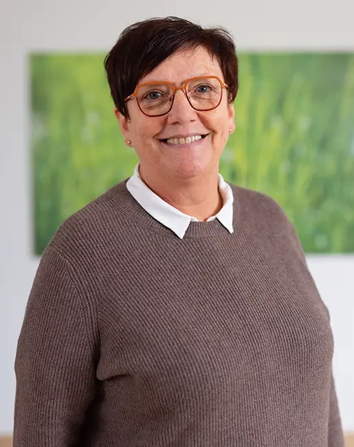 Bettina Löffler in braunem Pullover mit weißem Hemdkragen vor grünem Hintergrund