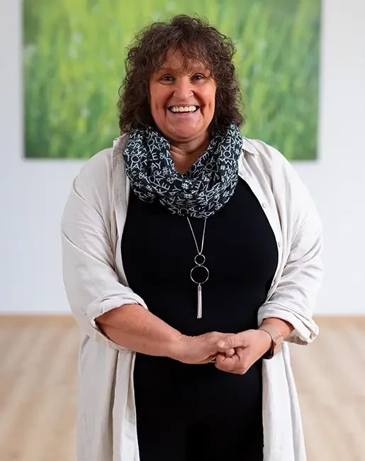 Nicole Schüttler in modernem Outfit mit Schal und Kette vor grünem Hintergrund