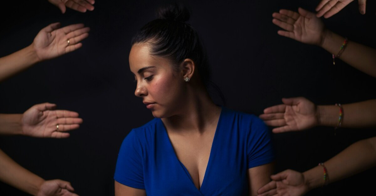 Burnout als Mutter – gestresste Frau in blauer Kleidung mit mehreren Händen, die sie erreichen