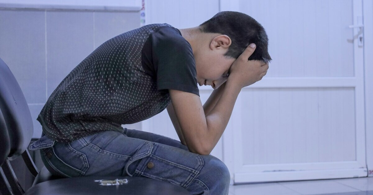 Überforderter Junge sitzt mit gesenktem Kopf und hält sich den Kopf in den Händen
