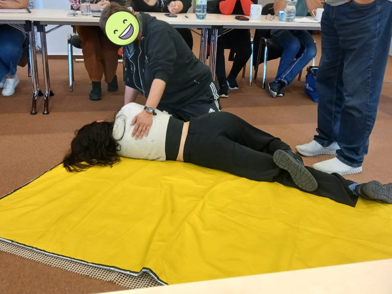 Sina und Lea bei einer Erste-Hilfe-Übung, stabile Seitenlage auf gelber Matte, im Seminarraum
