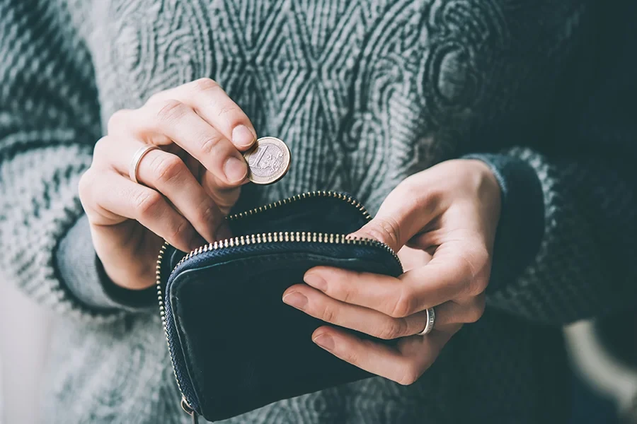Nahaufnahme einer Person, die eine Münze in einen Geldbeutel steckt – Symbolbild für private Insolvenz
