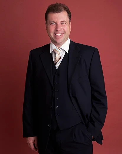 Jens Kunze aktuell im Anzug vor rotem Hintergrund