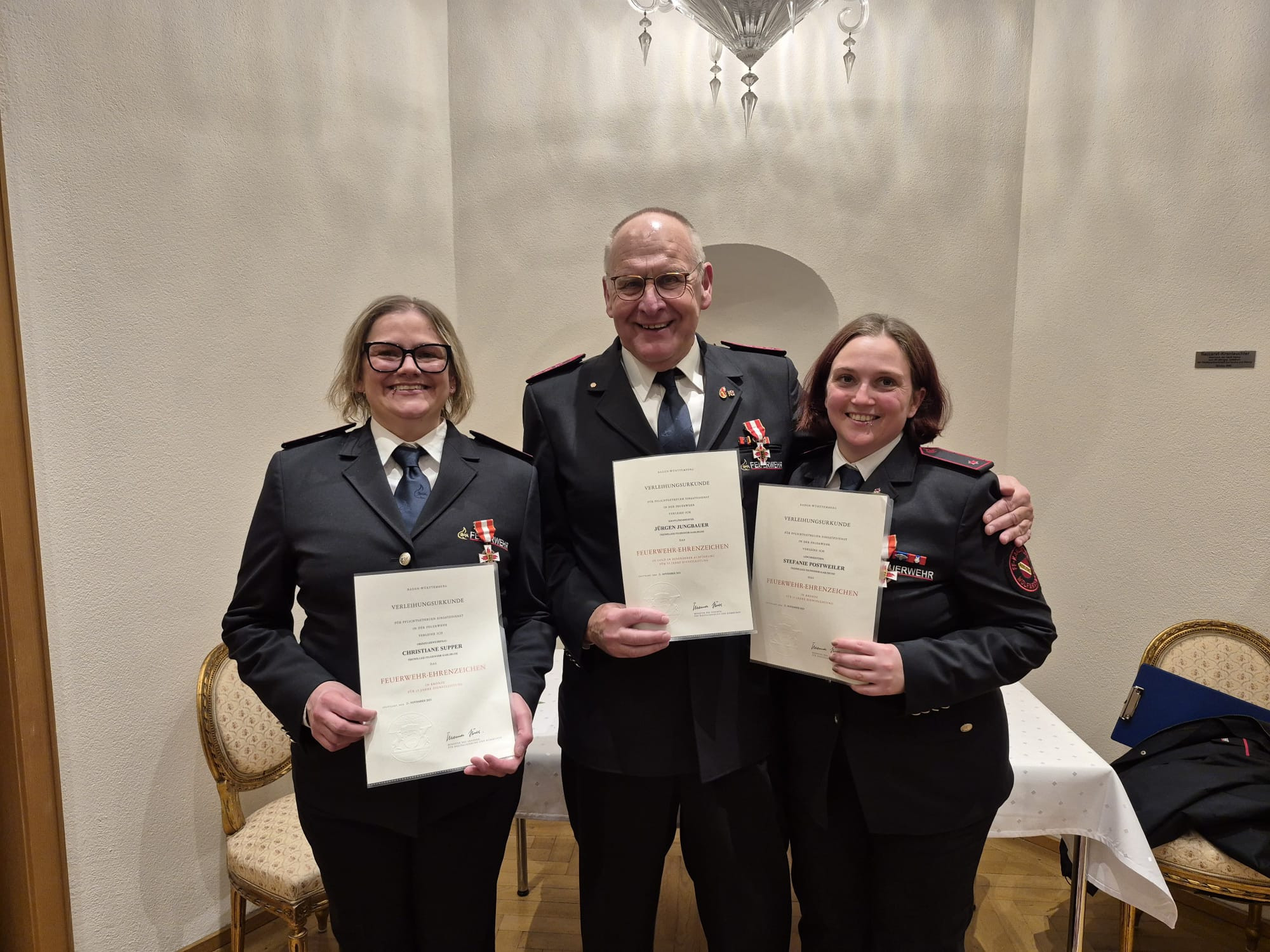 Verleihung des Feuerwehr-Ehrenzeichens an Steffi, Nane und Jürgen – drei Feuerwehrmitglieder in Uniform mit Urkunden und Ehrenzeichen