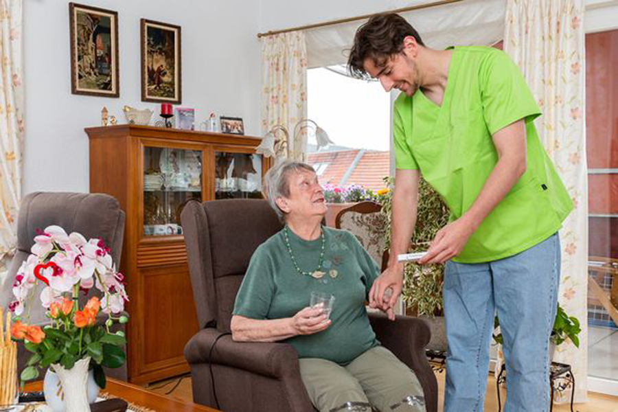 Pflegekraft betreut Seniorin im Wohnzimmer und reicht ihr ein Glas Wasser