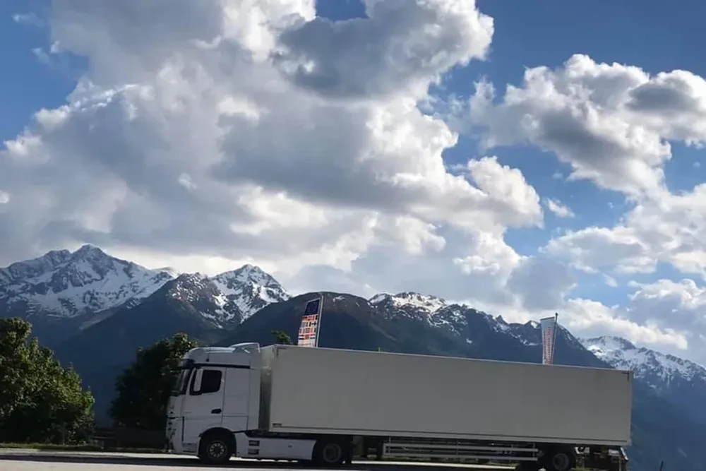 Weißer LKW vor verschneiten Bergen und bewölktem Himmel