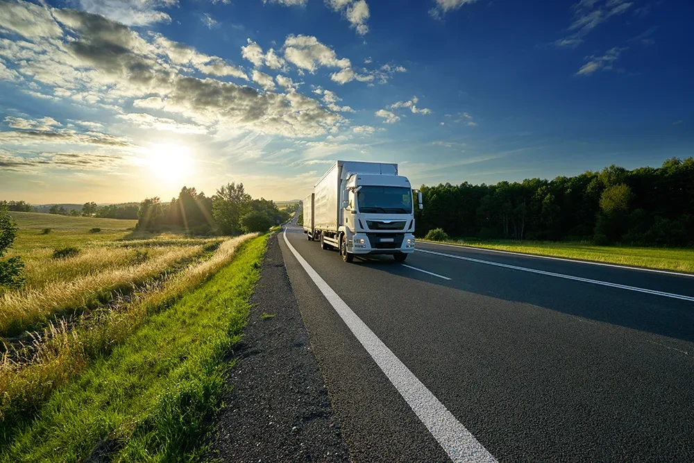 Moderner LKW fährt bei Sonnenuntergang auf einer Landstraße durch die Natur