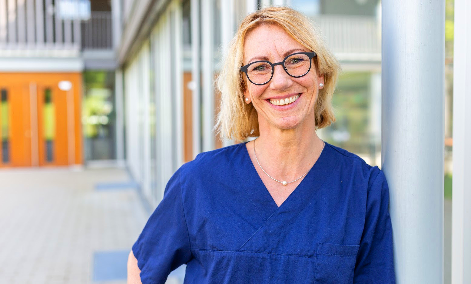 Astrid Kommert im blauen Kittel vor einem modernen Gebäude
