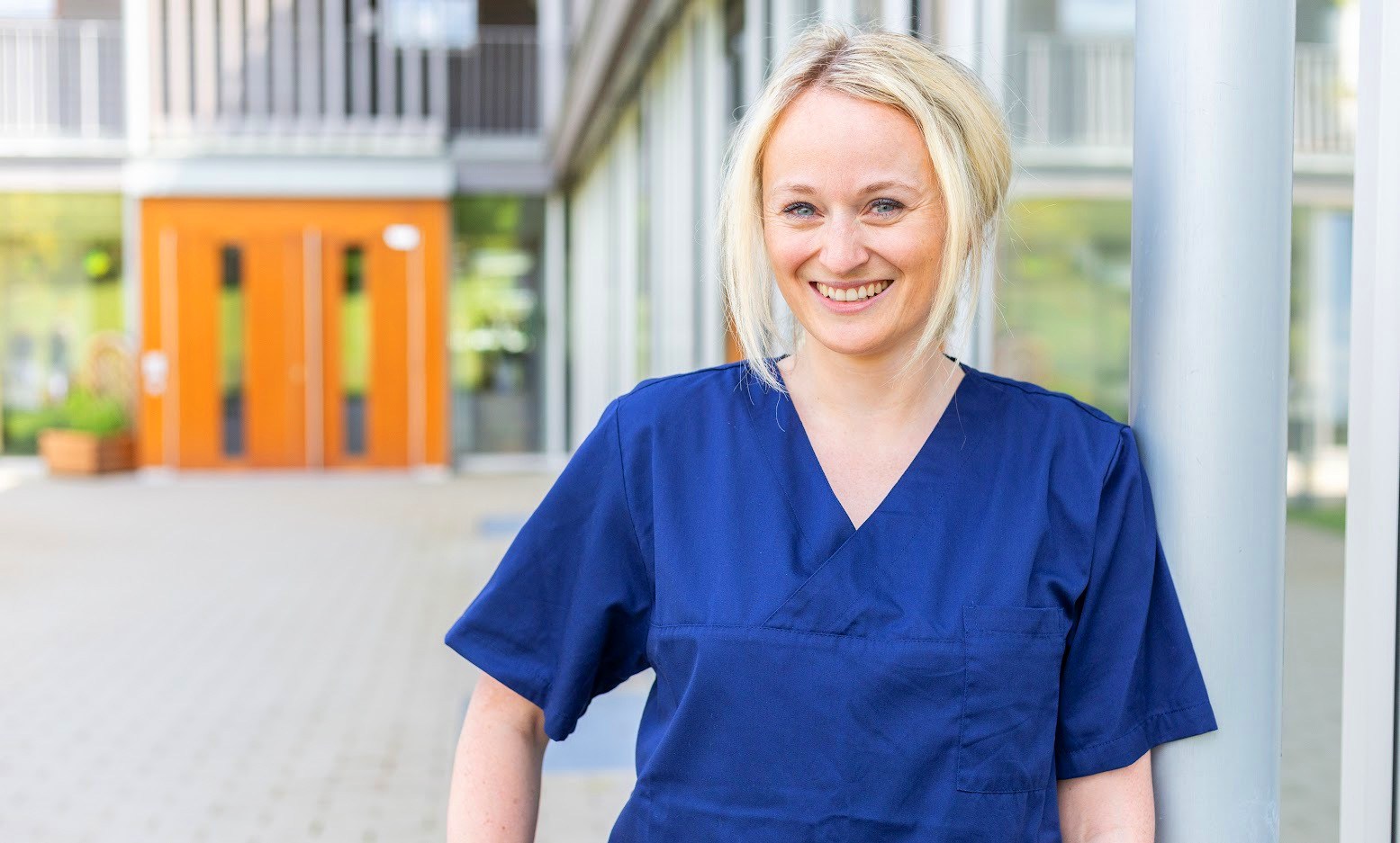 Dr. Sarina Mattner-Hess im blauen Arztkittel vor moderner Gebäudefassade