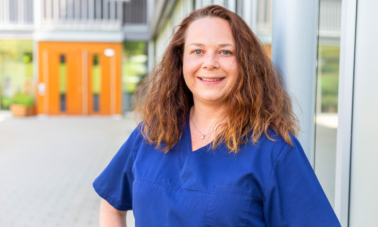 Jasmin Nalichofski in blauer Arbeitskleidung vor einem modernen Gebäude