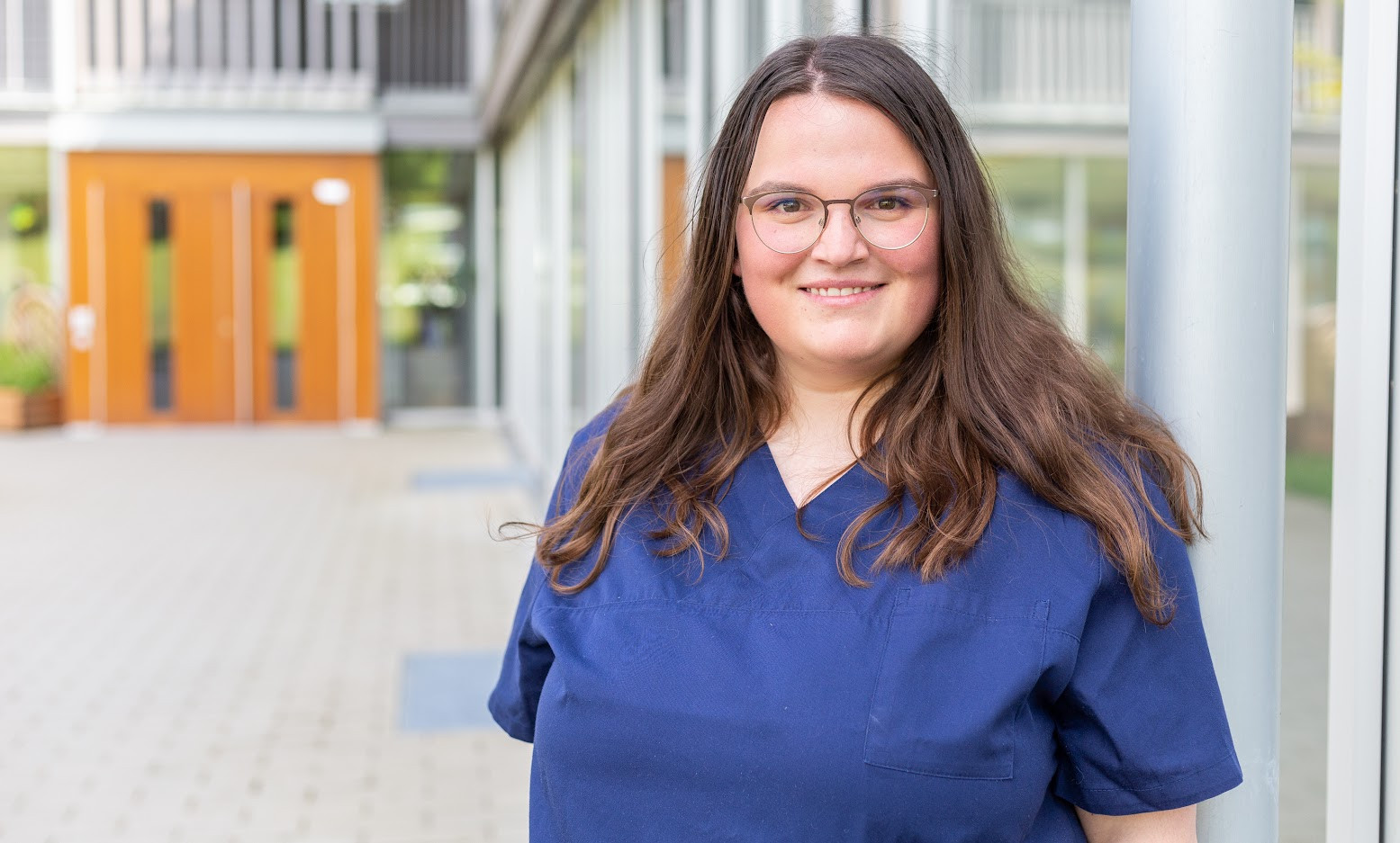 Jasmin Zoll in blauer Arbeitskleidung vor einem modernen Gebäude