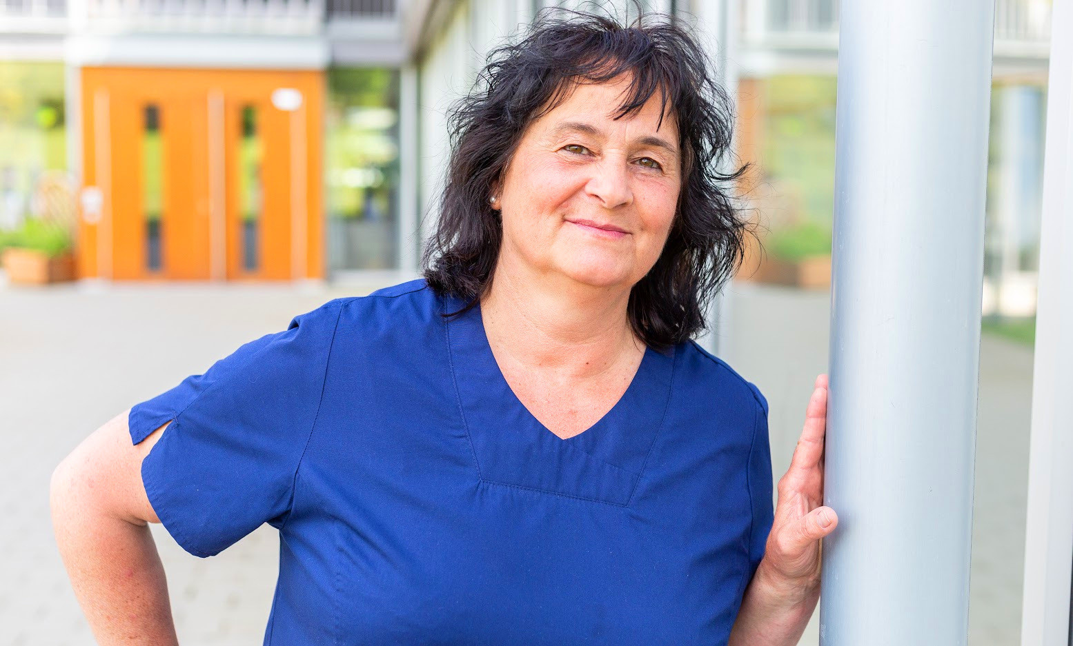 Silvia Riehle-Scherer in blauer Berufskleidung vor einem modernen Gebäude