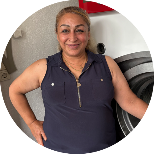 Maryan vor Waschmaschine mit dunkelblauem Oberteil Maryan steht vor einer Waschmaschine und trägt ein dunkelblaues ärmelloses Oberteil.