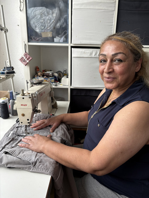 Schneiderin im Atelier an der Nähmaschine – Über uns Schneiderin arbeitet an einer Nähmaschine im Atelier – Über uns