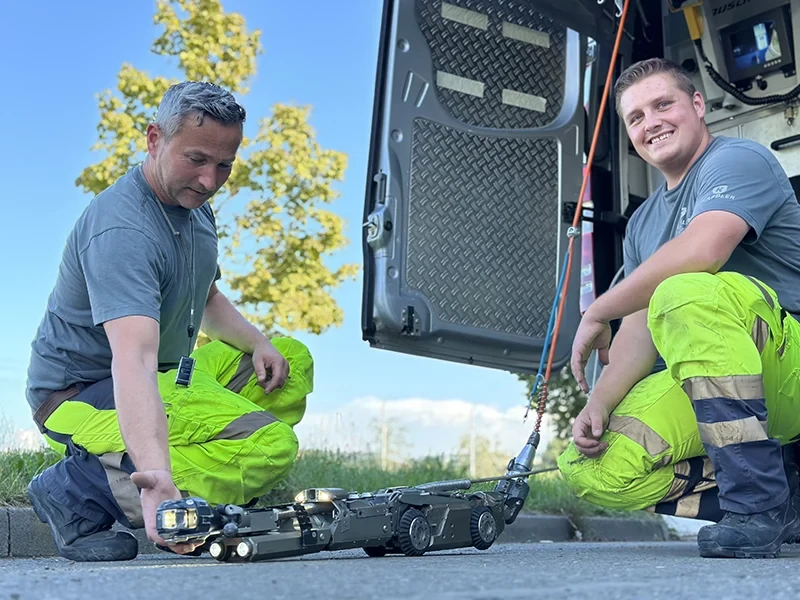 Zwei Arbeiter in Warnkleidung bedienen einen Inspektionsroboter vor einem Einsatzfahrzeug – startseite-header-bild-02.webp