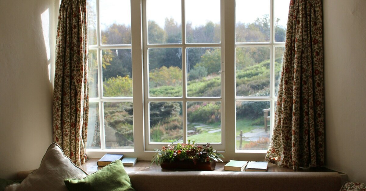 Fenster mit Ausblick auf einen grünen Garten und Landschaft im Hintergrund