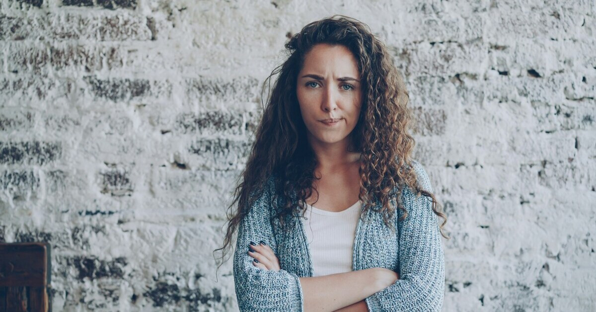 Genervte Person mit verschränkten Armen vor einer weißen Wand