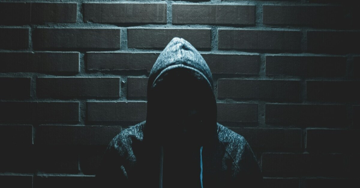 Gestalt im Schatten vor einer Ziegelwand, mysteriöse dunkle Silhouette mit Kapuze