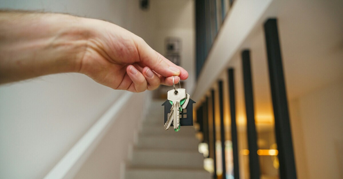 Hand hält Schlüssel vor Treppenaufgang – Symbol für Hausübergabe oder Einzug