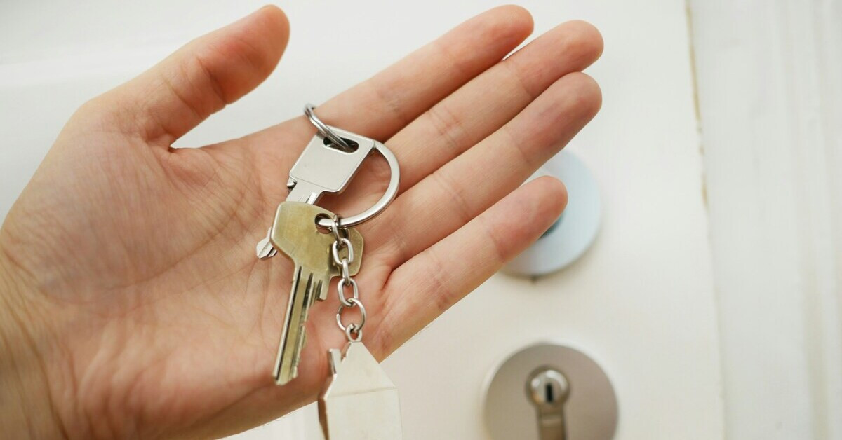 Schlüsselübergabe bei Wohnungsübergabe – Hand mit Schlüsselbund vor Haustürschloss