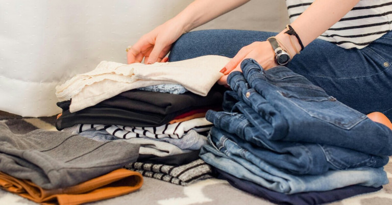 Kleidung ausmisten und organisieren – Tipps zum Kleiderschrank ausmisten Kleidung ausmisten: Frau sortiert und faltet Kleidung zum Ausmisten und Organisieren des Kleiderschranks