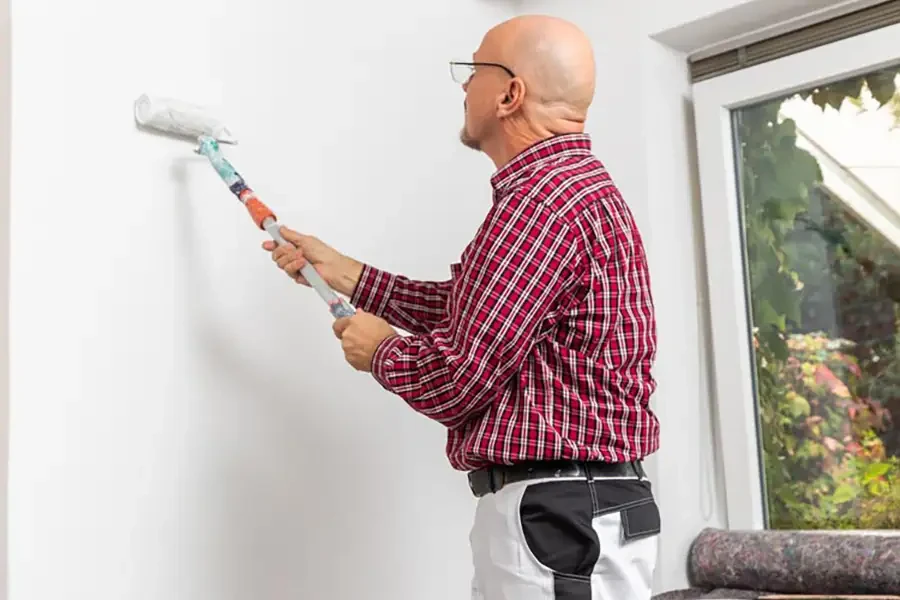 Maler bei der Arbeit: Wand streichen mit Farbrolle – teaser malern Maler streicht mit Farbrolle eine weiße Wand – teaser malern