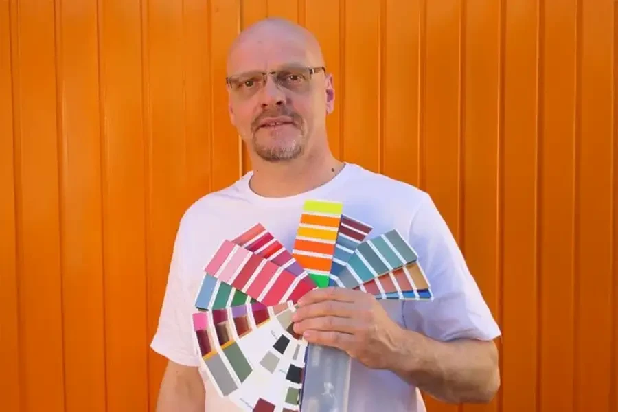 Michael Bruder präsentiert Farbfächer vor orangefarbener Wand Michael Bruder mit Farbfächer vor orangefarbener Wand