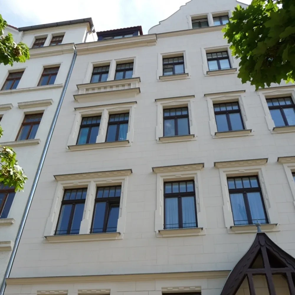 Fassadenansicht eines mehrstöckigen Wohnhauses mit weißen Wänden und großen Fenstern, fotografiert im Sommer