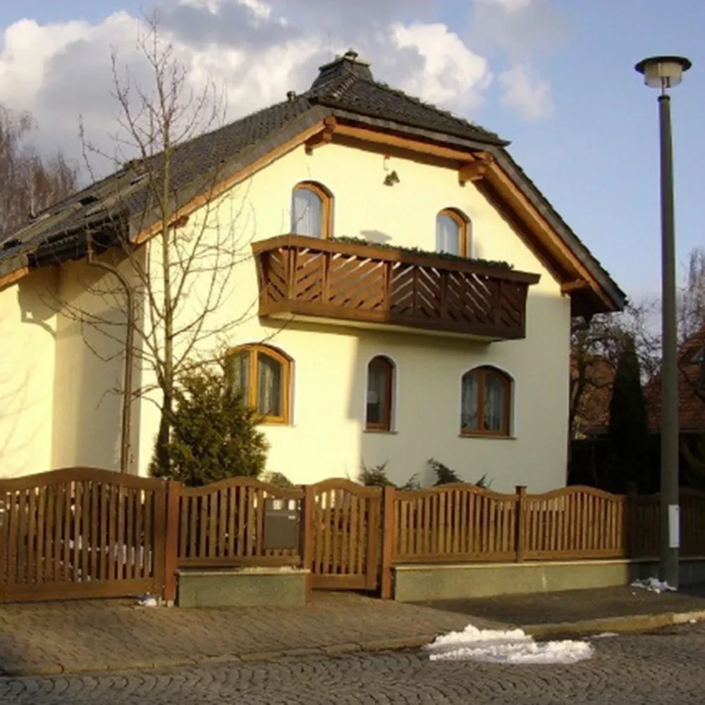 Modernes Einfamilienhaus mit Holzbalkon und Zaun, aufgenommen bei Tageslicht