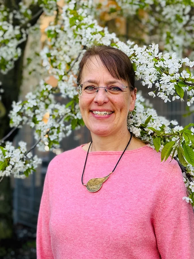 Thiel vor blühendem Baum im Frühling, lächelnde Frau mit Brille und rosa Pullover