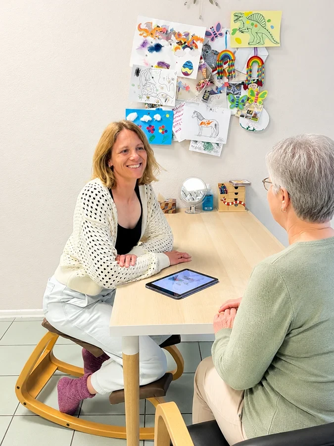 Erwachsene Frauen im Beratungsgespräch an einem Tisch mit Tablet und Kinderzeichnungen im Hintergrund