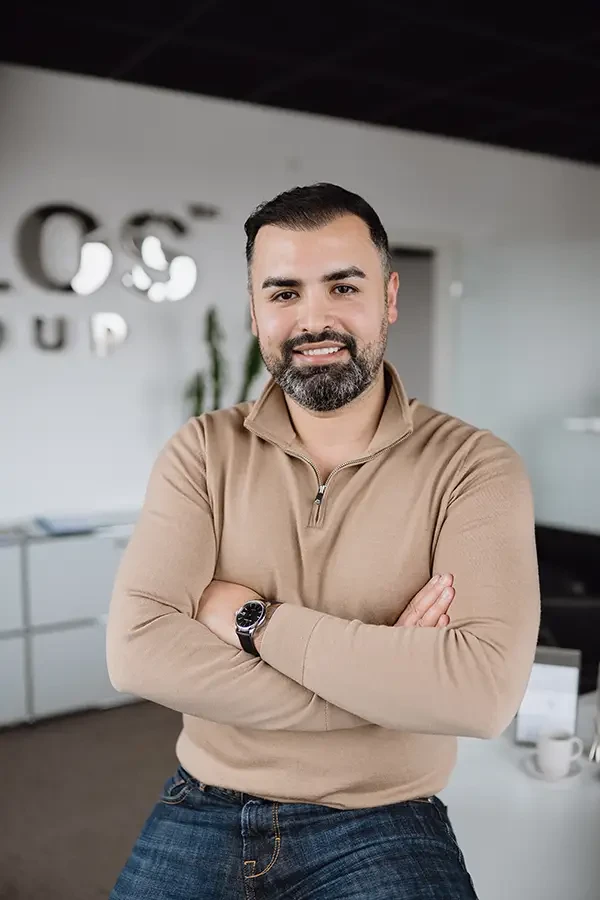 Geschäftsmann mit beigem Pullover steht mit verschränkten Armen im modernen Büro