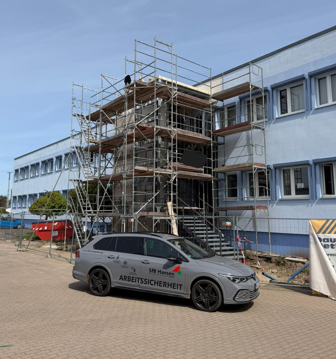 Baustelle mit Gerüst und Pkw der Firma Sfb Hansen Arbeitssicherheit vor einem Bürogebäude
