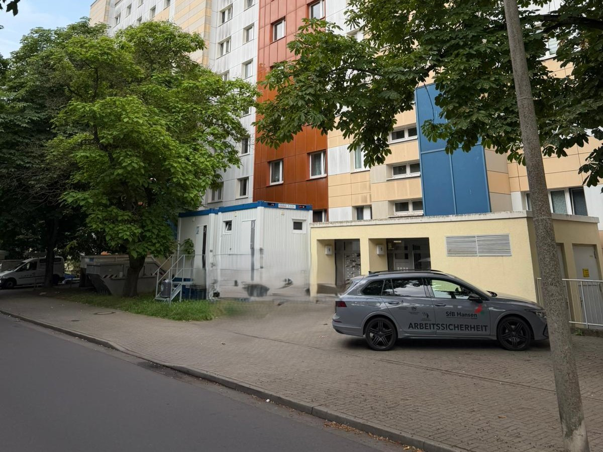 Mehrfamilienhaus an der Grundigstraße während einer Strangsanierung mit Baustellencontainer und Fahrzeug für Arbeitssicherheit vor dem Gebäude
