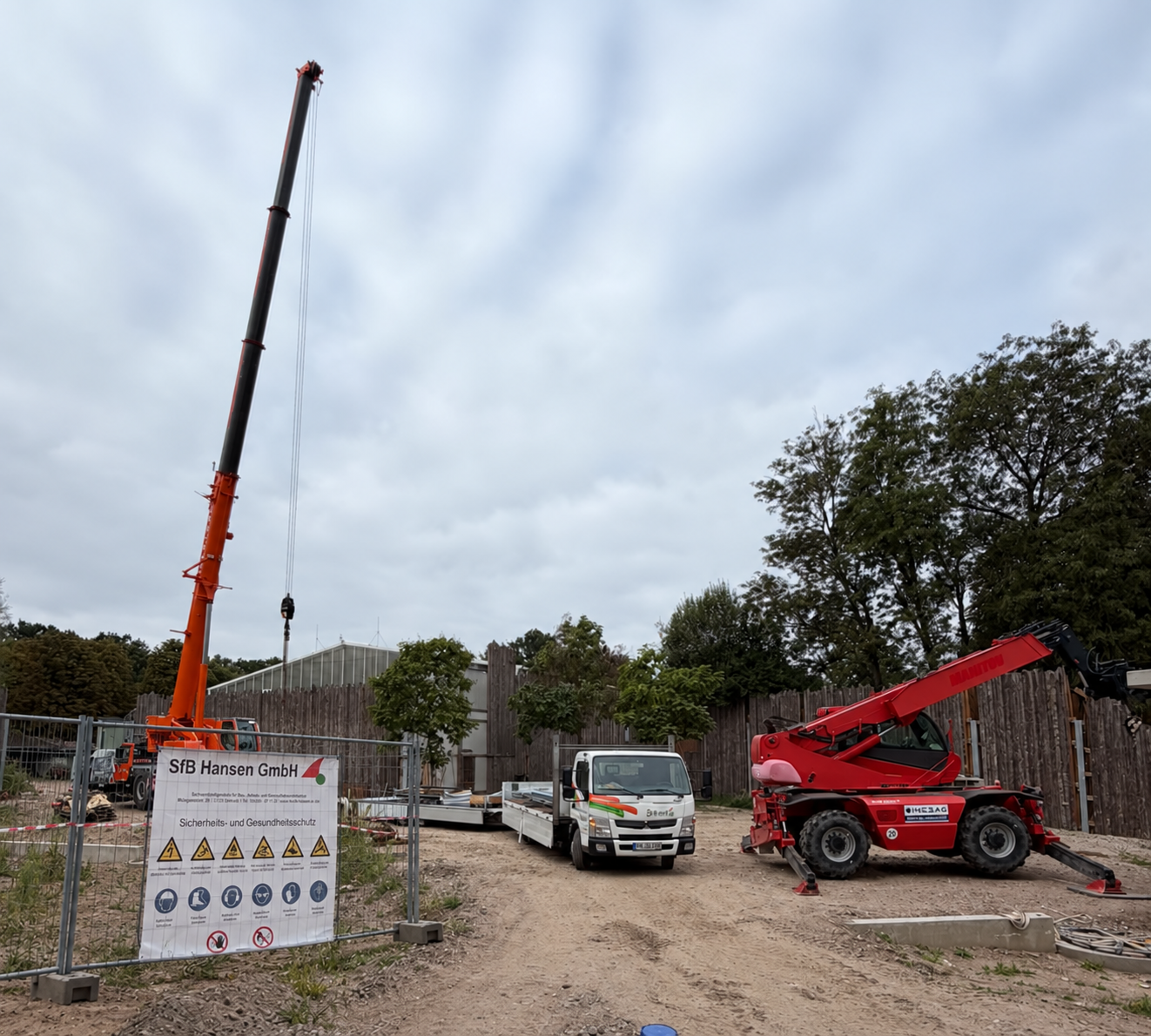 Baustelle im Zoo mit Kran, LKW und Bagger vor einem Gehege, Schild der SFB Hansen GmbH im Vordergrund