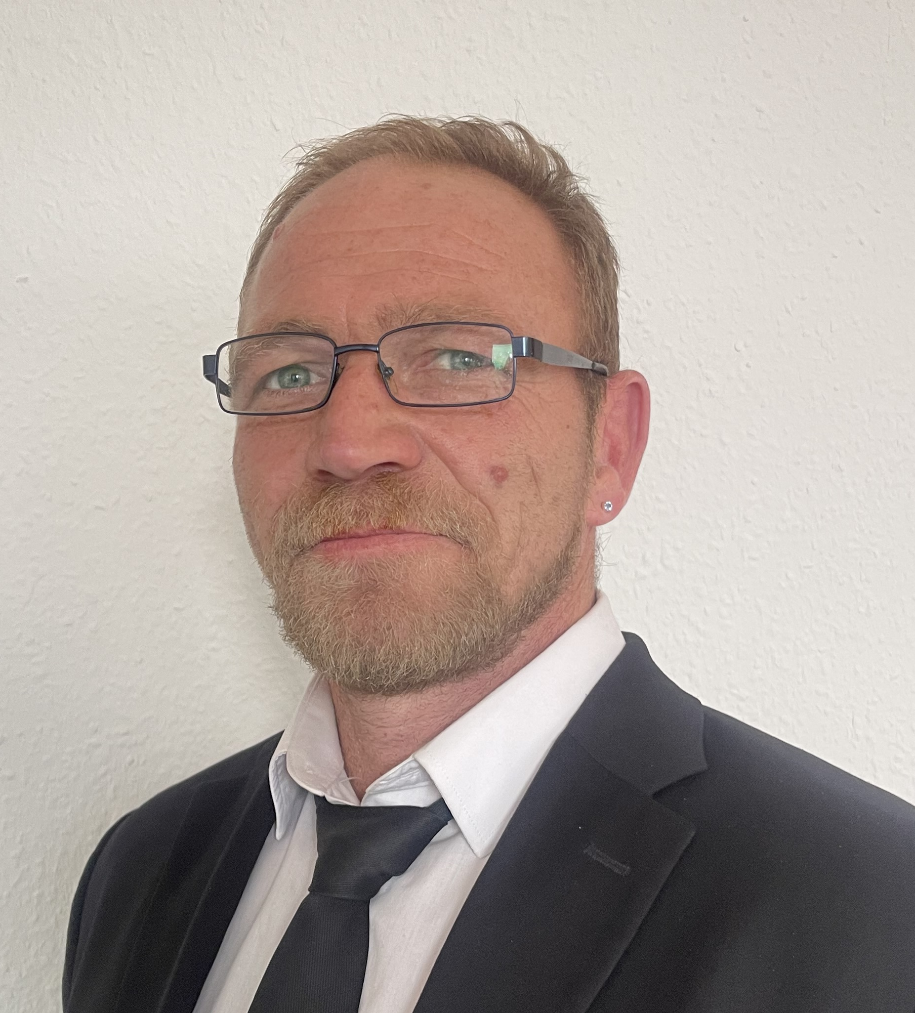 Herr Neumann von Abendfriede im Anzug und Krawatte vor hellem Hintergrund