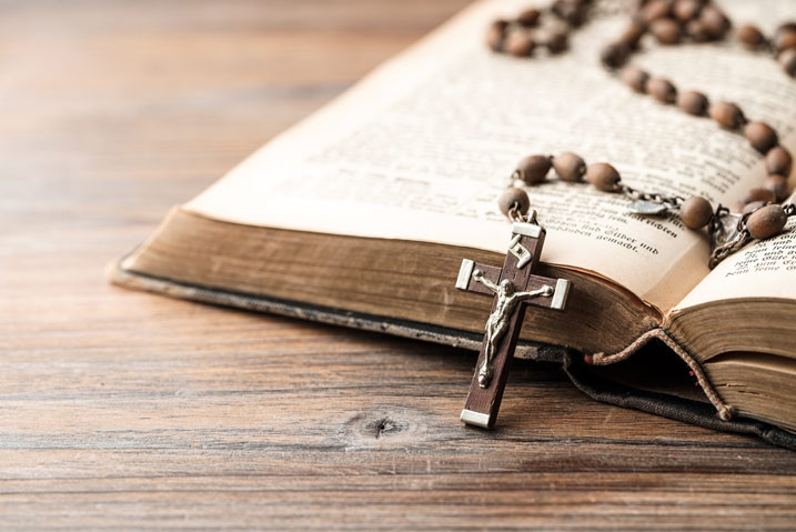 Teaser Über uns – Nahaufnahme einer Bibel mit Rosenkranz auf Holztisch