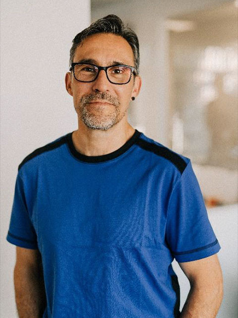 Ruediger Pach in blauem T-Shirt stehend vor unscharfem Hintergrund