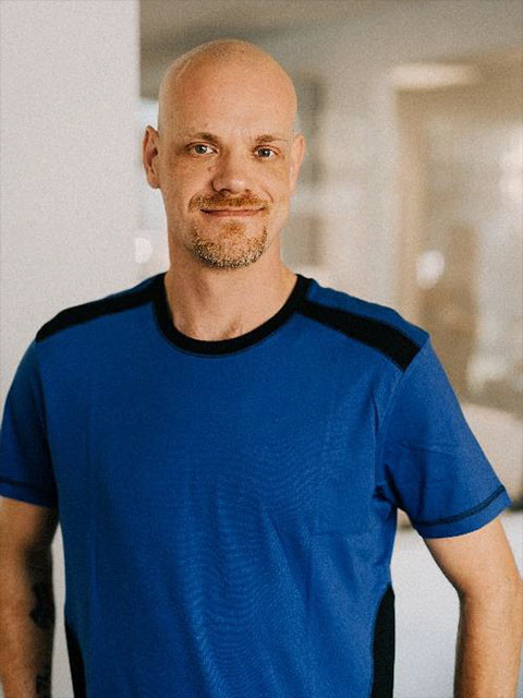 Marc Fischer in blauem T-Shirt vor unscharfem Hintergrund