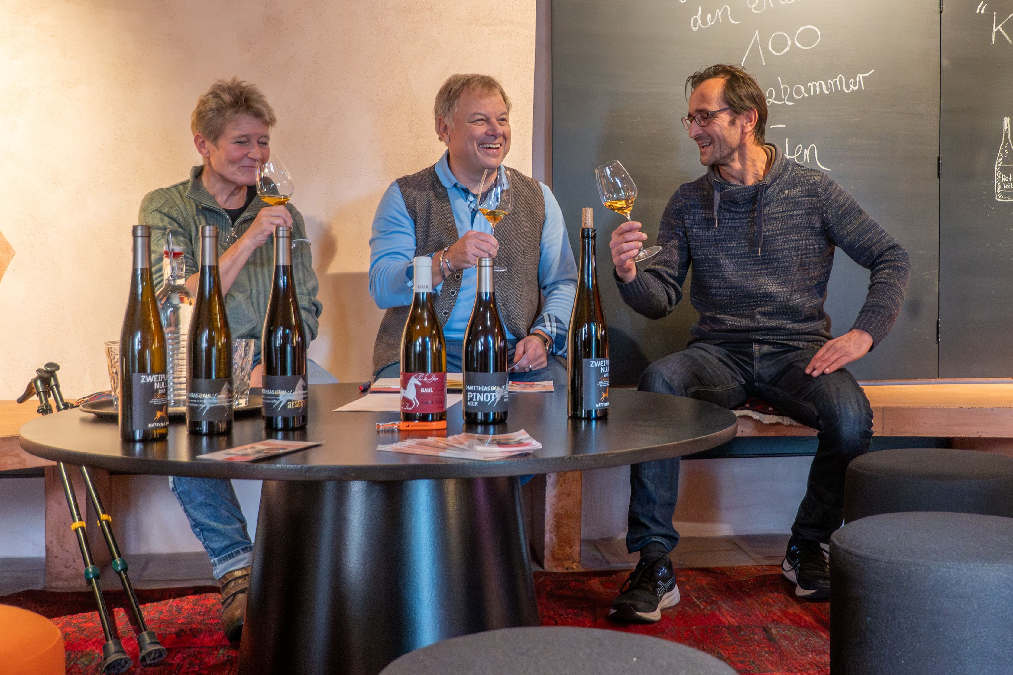 Weinprobe mit verschiedenen Weinpaketen vom Weingut Gaul auf einem Tisch, mehrere Personen verkosten Wein