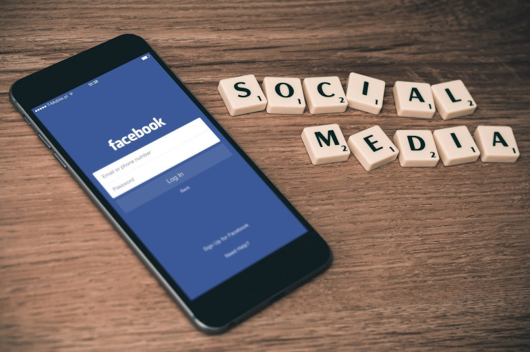 Smartphone mit Facebook-App und Scrabble-Buchstaben 'Social Media' auf Holztisch
