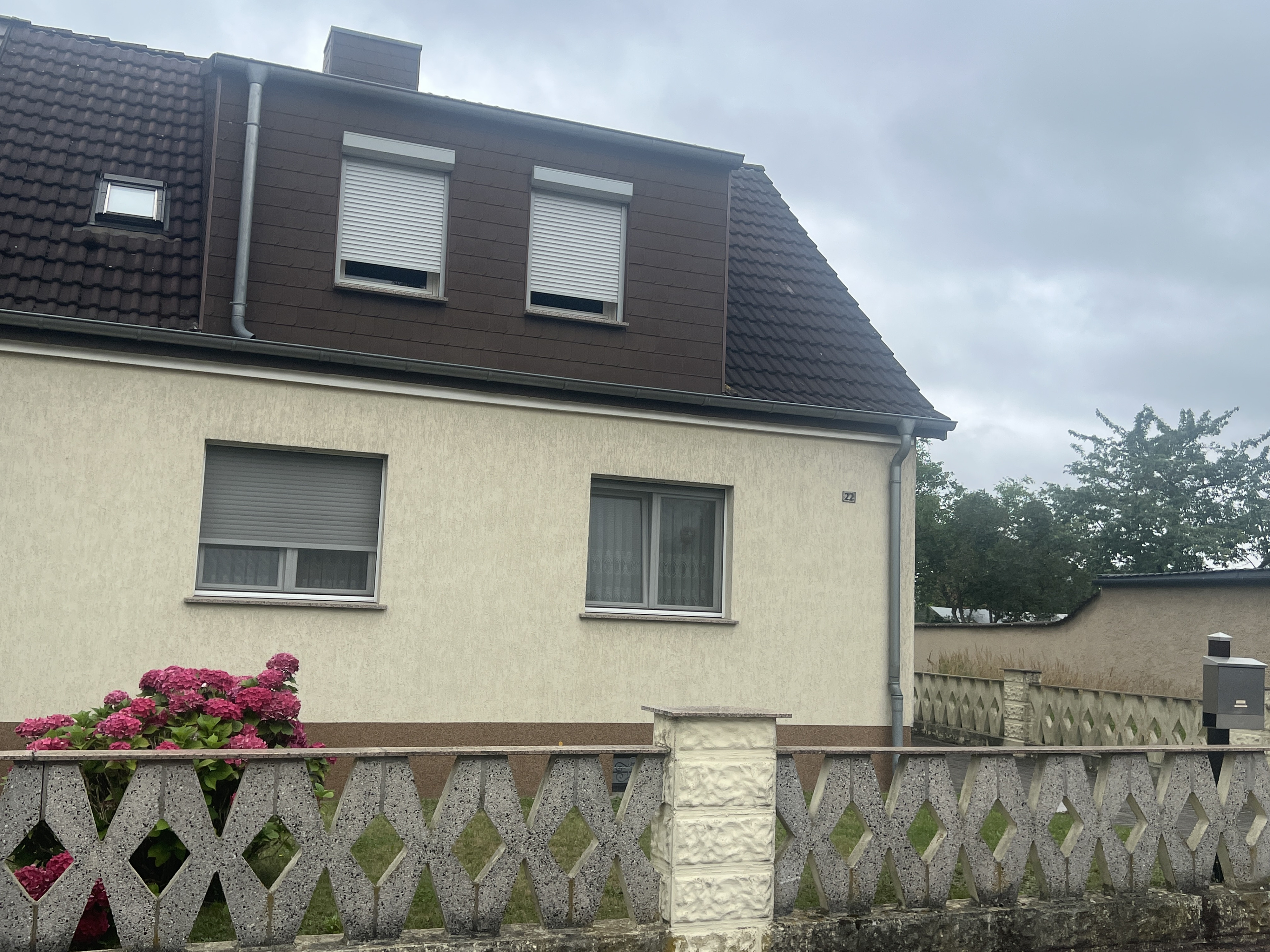 Einfamilienhaus mit Vorgarten und Betonzaun an einem bewölkten Tag